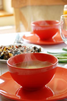 red plates with hot soup served on table in kitchen for dinner