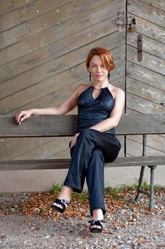 Beauty, mature woman sitting lean on old wooden board wall.