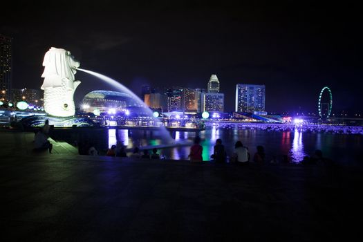 A view of singapore at night with the merlion in the foreground