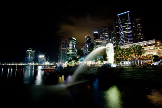 A view of singapore at night with the merlion in the foreground