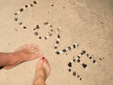 Letters of love by stones in sand, with male and female feet