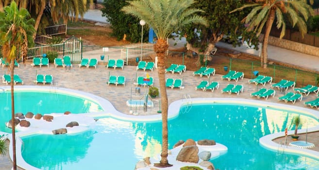 Swimming pool overview, with palm-trees and sun-beds