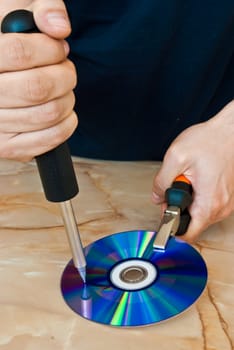 Man destroying a compact disc with a screwdriver