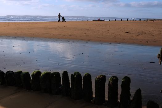 parent pushing a pushchair with child running in the sandy beach