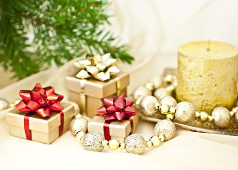 The gold background with a Christmas candle ball chains and gift boxes, a back background fir twig.
