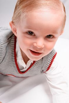 A child portrait of ahandsome toddler dressed in nice clothing and is crawling and smiling at the viewer