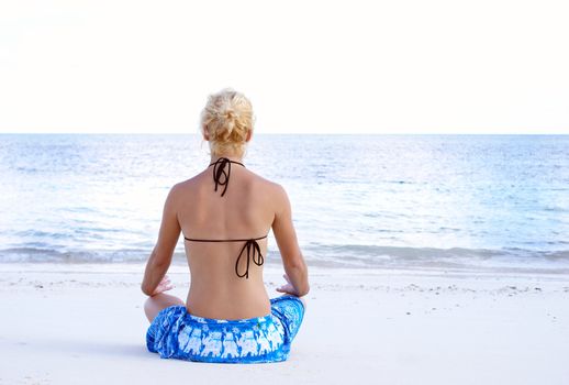 A young girl is meditating on the beach.