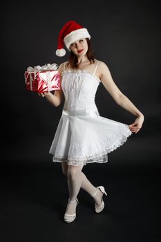 A girl in a red Christmas hat with gifts on dark background