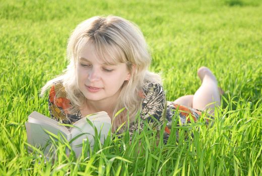 Young beautiful girl reading a book outdoor in green grass