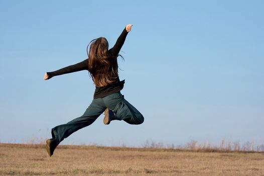 Happy girl jumping around on dry field