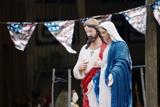 Kitsch statues of jesus and Mary in front of an American Flag banner
