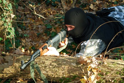 terrorist in camouflage aiming with his rifle outdoor in forest