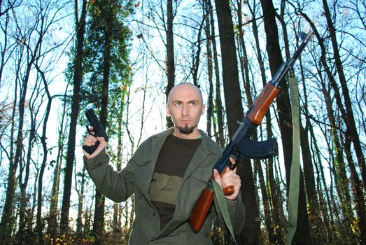 young man impersonating revolutionary in the forest with guns