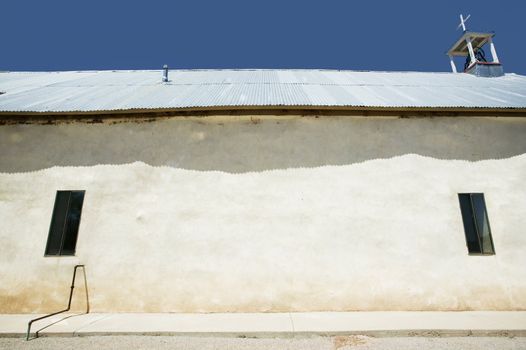 Side of rustic adobe church with corrugated metal roof