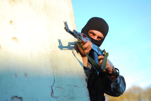 terrorist with mask hidden behind a wall and aiming with his gun