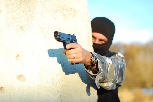 terrorist with mask hidden behind a wall and aiming with his gun