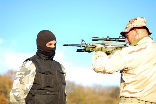 US soldier taking armed criminal under arrest with blue sky behind