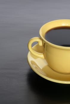 Closeup of yellow cup with hot black coffee on dark background