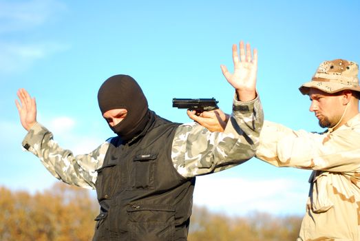 US soldier taking armed criminal under arrest with blue sky behind