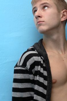 Young guy looking up standing on blue wall background. No glamour, natural