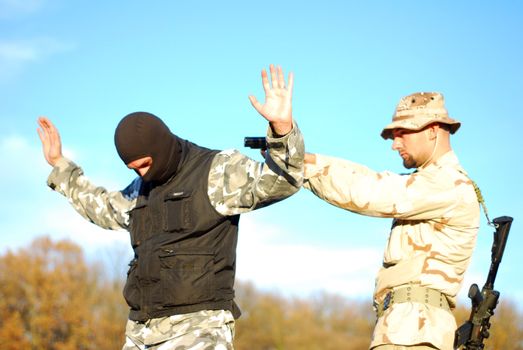 US soldier taking armed criminal under arrest with blue sky behind