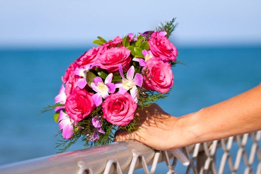Close up of a  beautiful vibrant wedding boquet held by the bride in front of a blue ocean