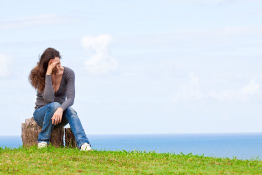 Photo of a depressed and upset young woman sitting outside with her head in her hands