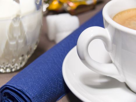 A cup of coffee with foam, milk, sugar and a blue napkin