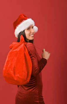 Beautiful Christmas girl with gifts sack against a red background.