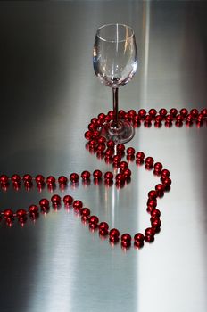 Wine-glass and red beads on a metal background