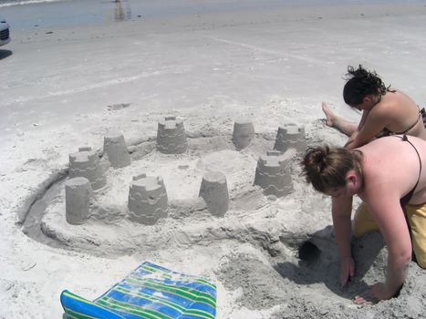 Two people are building sand castles at a public beach.