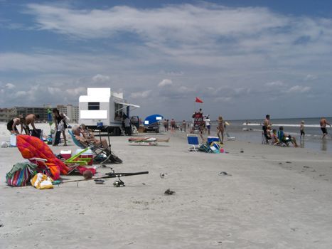 People are all over the beach relaxing while some are swimming in the ocean on a somewhat cloudy day.