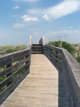 A long walking trail leading to the beach has a blue sky as a background