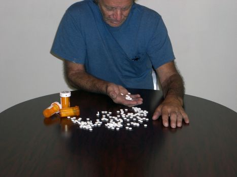 A sad looking man is holding prescription pills in his hand, and some are scattered in front of him.