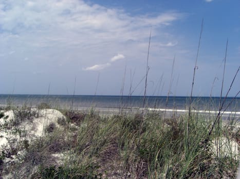 A heap of sand dunes are formed at the beach with a background of an ocean, horizon and blue skies.