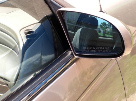 This is a side mirror of a Ford Taurus, and it reflects the interior of the car, a house, trees and a lawn.
