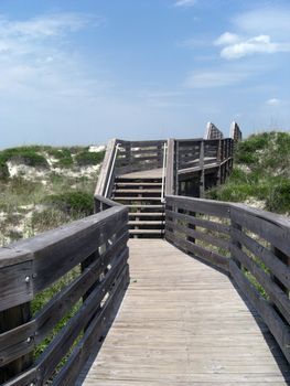 A winding trail that is leading to the beach has a blue sky as a background