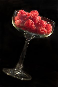 Raspberries presented in a glass bowl on black background