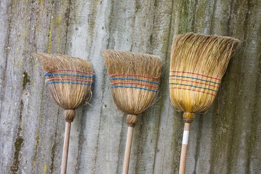 three used brooms on a concrete wall