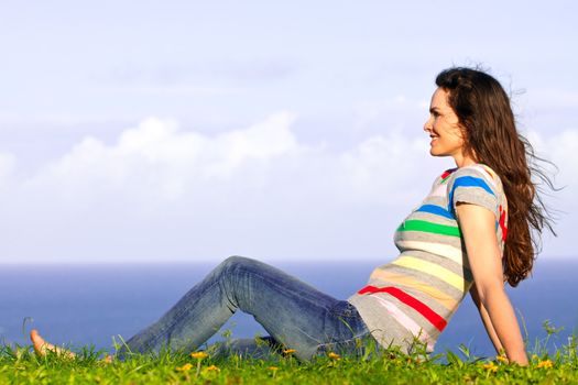 A beautiful young happy woman relaxing in the grass by the ocean