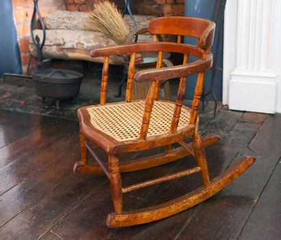 Wooden rocking chair for child standing by old fireplace in 19th century house