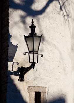 Black street lamp casts a shadow on an old stone wall