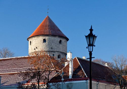 Tower on the town walls in Tallinn in Estonia in winter with snow on red tiled roofs and ornate lamp in foreground