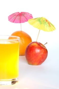 Orange and apple with small paper sunshades near glass of fruit juice on white background