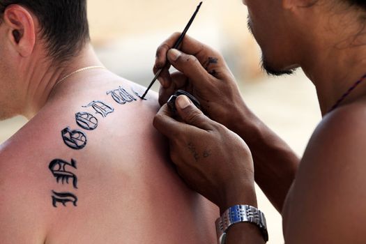 Artist draws a tattoo henna on a man's back