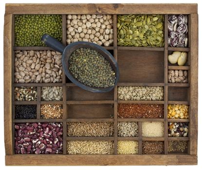 rustic scoop of French green lentils  and a variety of beans, lentils, seeds in old wooden typesetter case, isolated with clipping path