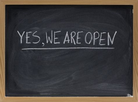 "yes, we are open" - business invitation handwritten with white chalk on blackboard with eraser smudges