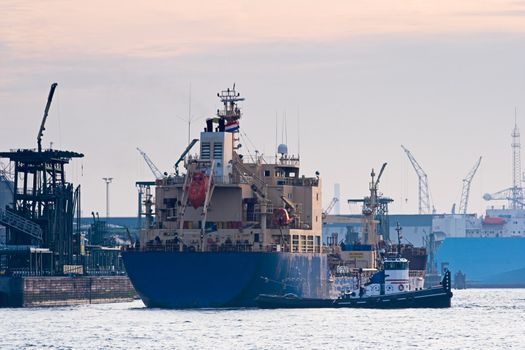 Tanker in harbour, pulled by a tug, is mooring to the quay