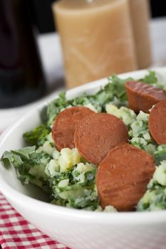 Dutch stamppot, mashed potatoes with kale, topped with vegetarian sausage. Vertical orientation.