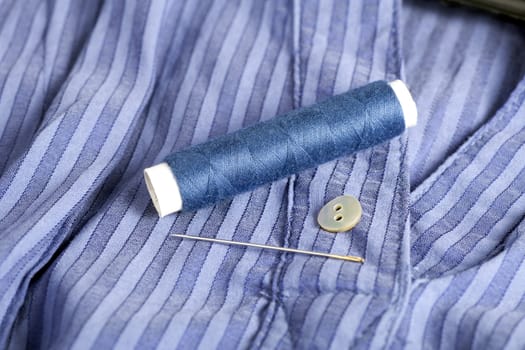 Blue shirt with button, thread and sewing needle ready for mending.